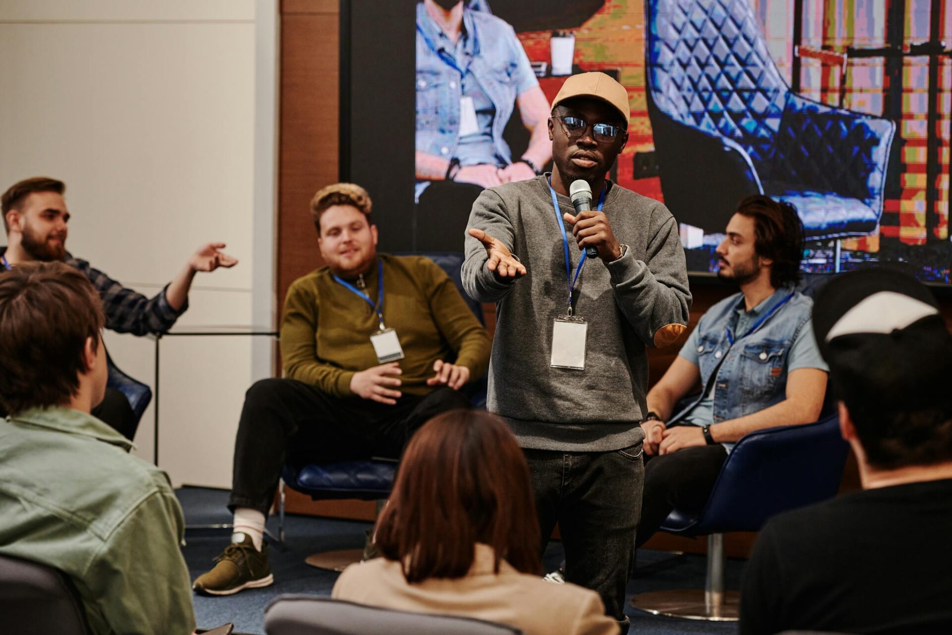 A confident young man speaking at a conference, engaging with an audience in an indoor setting.